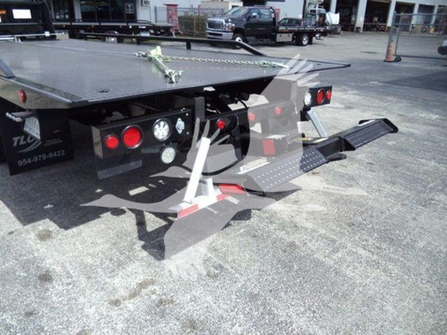 Flatbed tow truck rear with ramps extended and taillights visible.