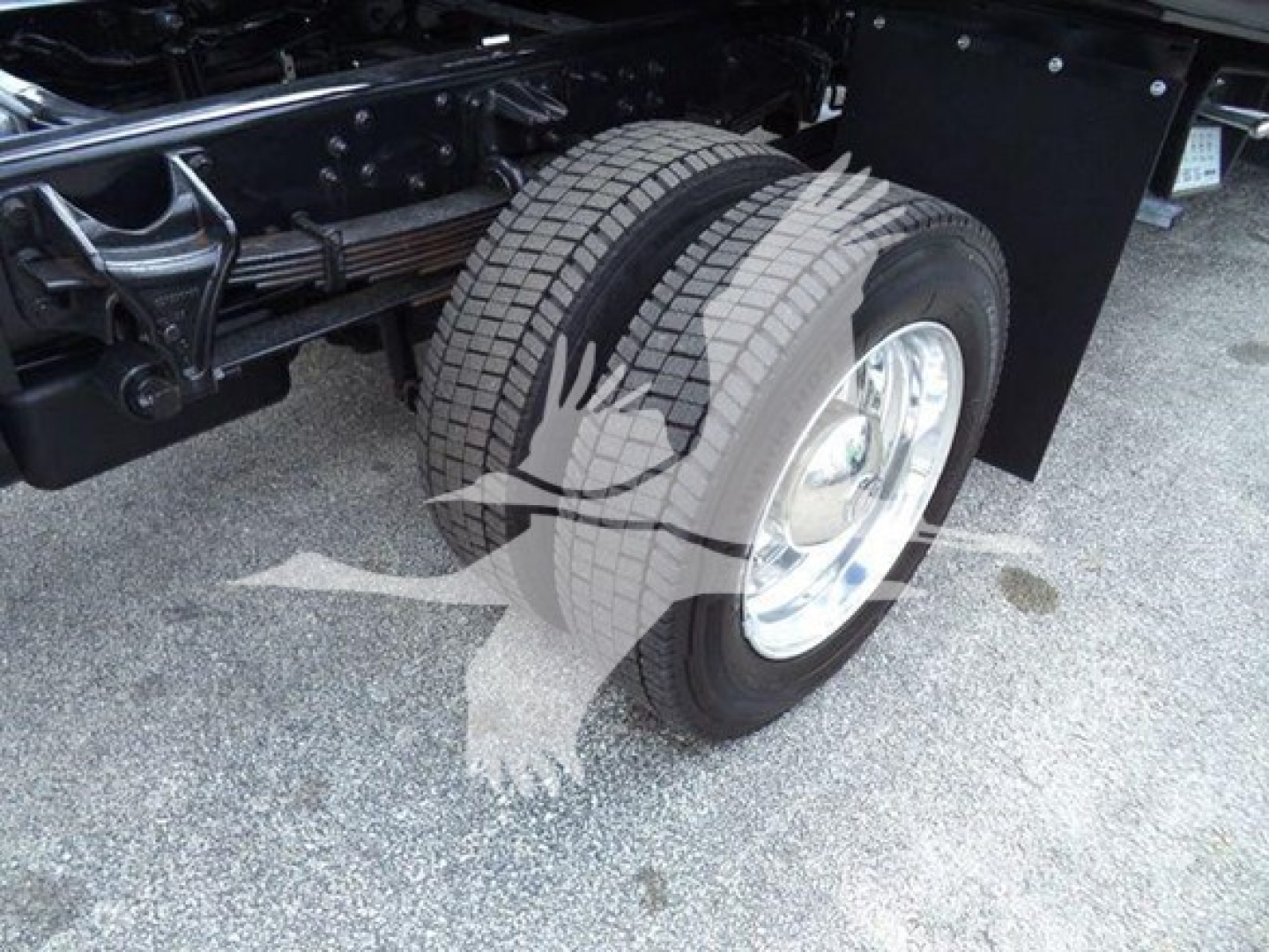 Truck rear wheel and suspension undercarriage with matching dual tires and chrome wheel; visible components include leaf spring, axle, and frame. No readable text present.