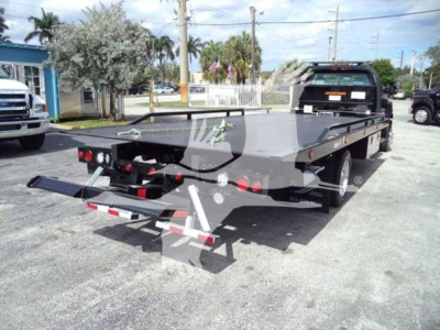 Flatbed tow truck in a dealership lot with rear view showing winch and dual rear wheels.