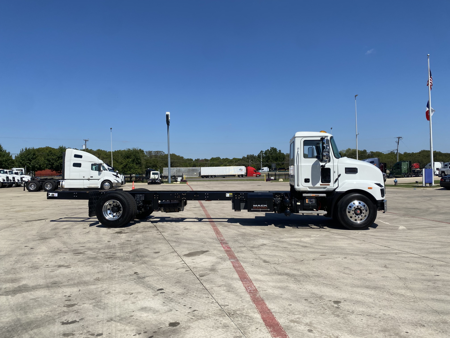 Mack MD6 E cab and chassis truck in a parking lot displaying a long wheelbase with a flatbed frame and front cab, side view.
