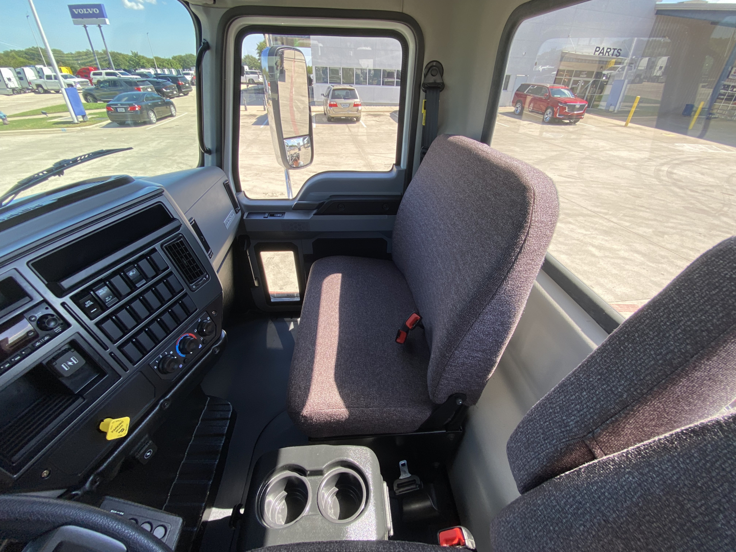 Cab interior of a 2024 Mack MD6 E truck showing driver and passenger seats, dashboard with controls, and cup holders.