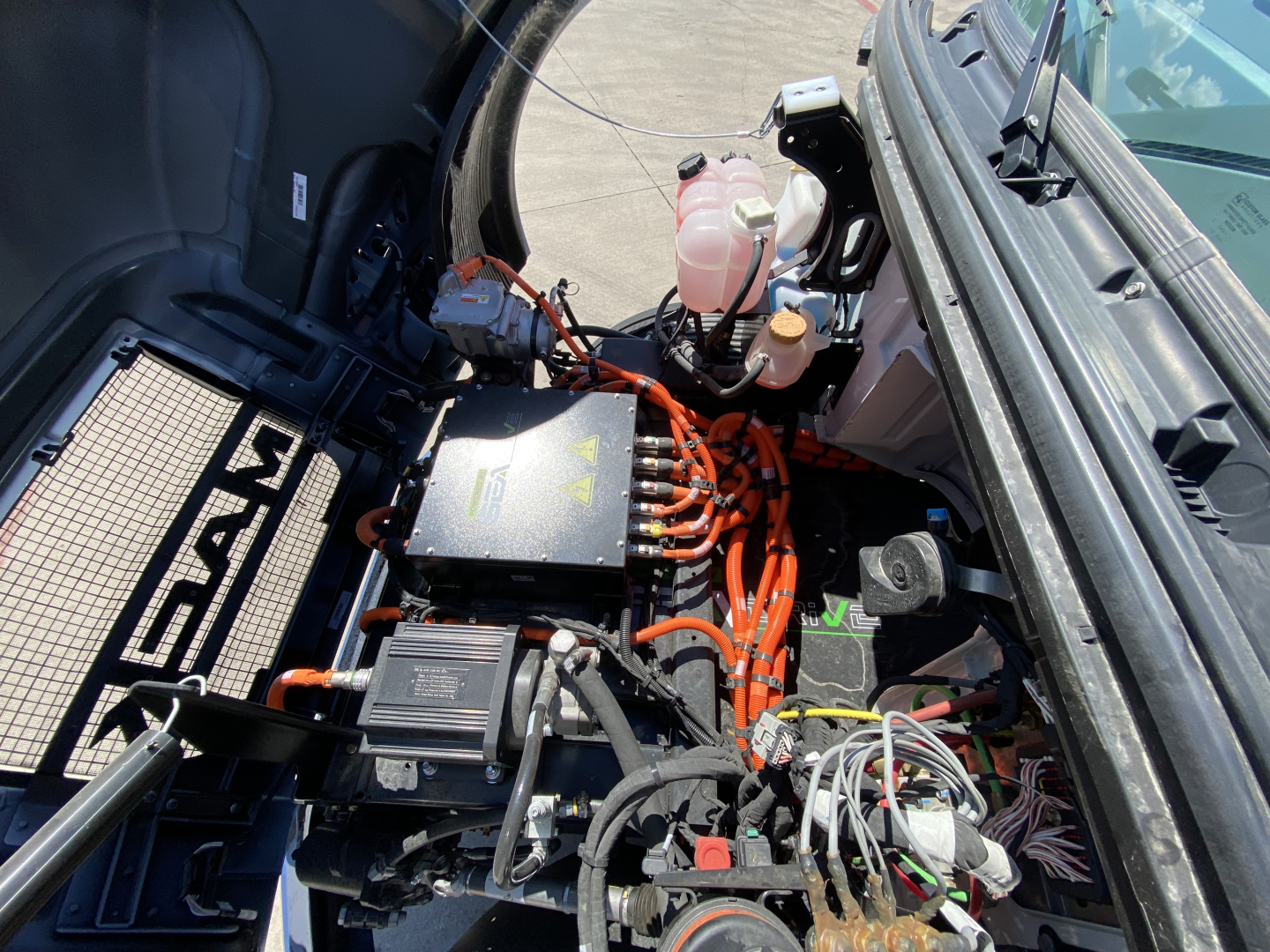 Cab and chassis engine bay of a 2024 Mack MD6 E showing orange high-tension cables, air intake components, coolant reservoir, and electrical harnesses.