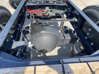 View of a Mack MD6 chassis bay with rear differential housing, suspension links, hydraulic lines, and frame rails visible; engine bay mostly clear, no engine present.