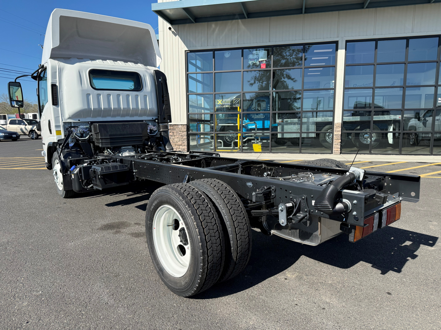Isuzu NPRXD cab and chassis with exposed drivetrain and chassis rails, front wheel, and cab in background.