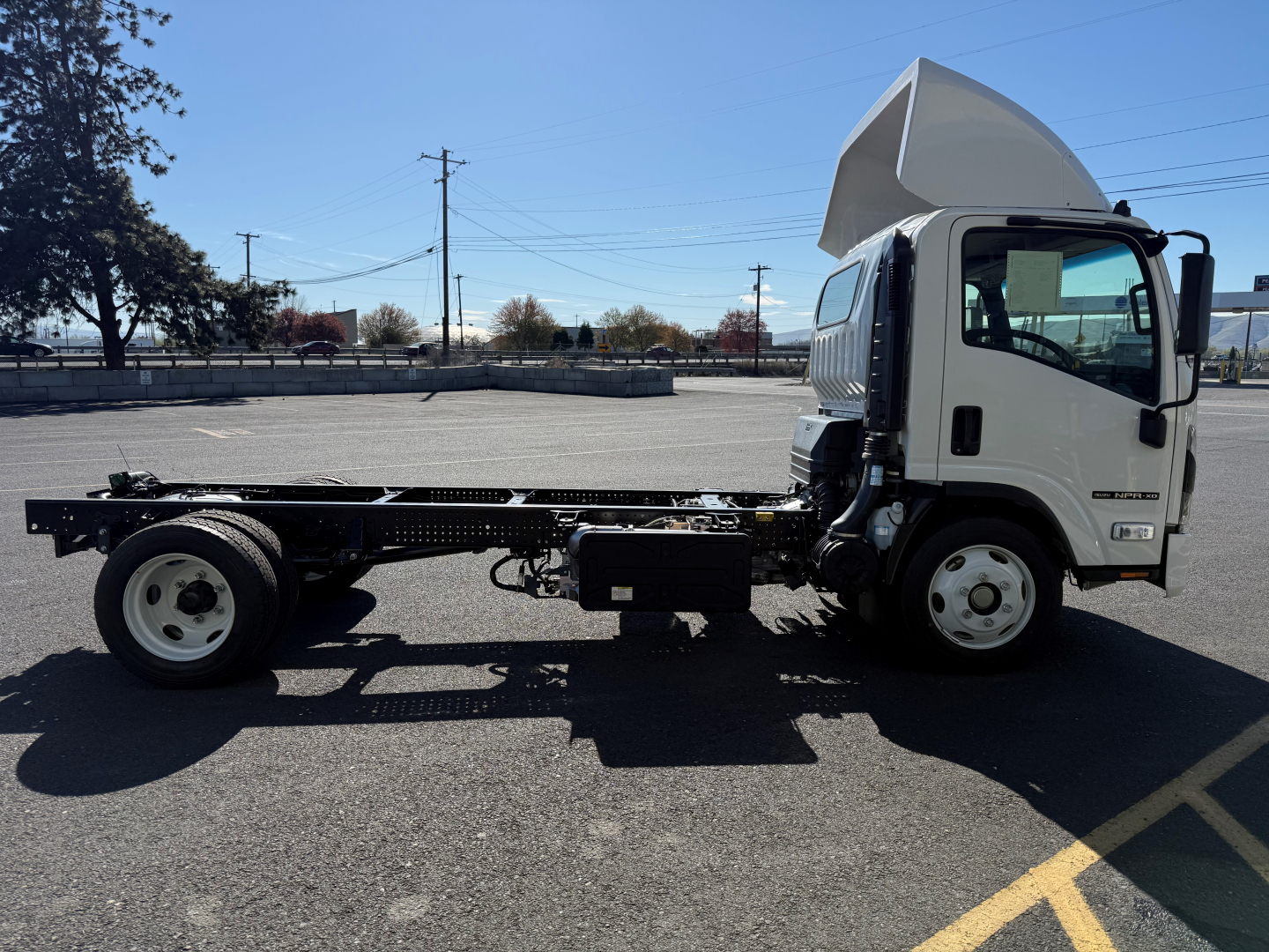 Isuzu NPRXD cab and chassis side view showing empty flatbed frame and cab, white cab, open chassis with wheelbase, signage not visible.
