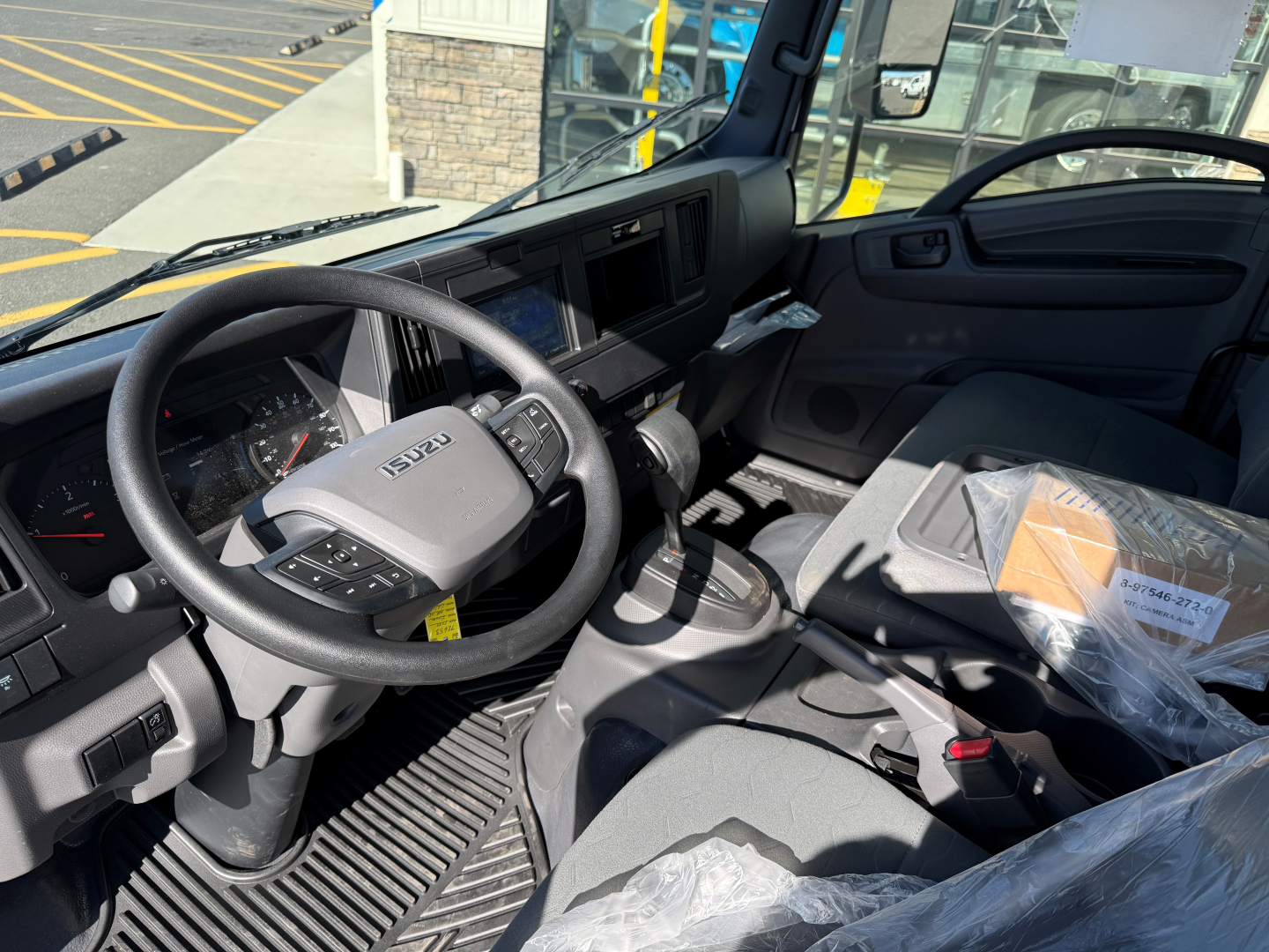 Isuzu NPRXD cab and chassis interior showing steering wheel, dashboard, and driver seat with plastic-wrapped components.