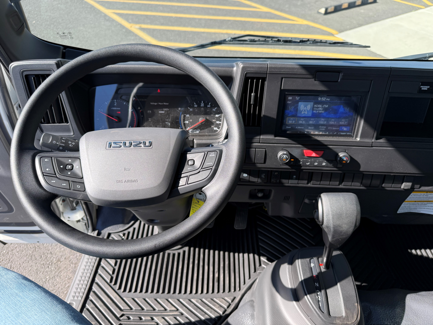 Isuzu NPRXD cab interior showing steering wheel with Isuzu logo, dashboard, gear selector, and touchscreen infotainment/display.
