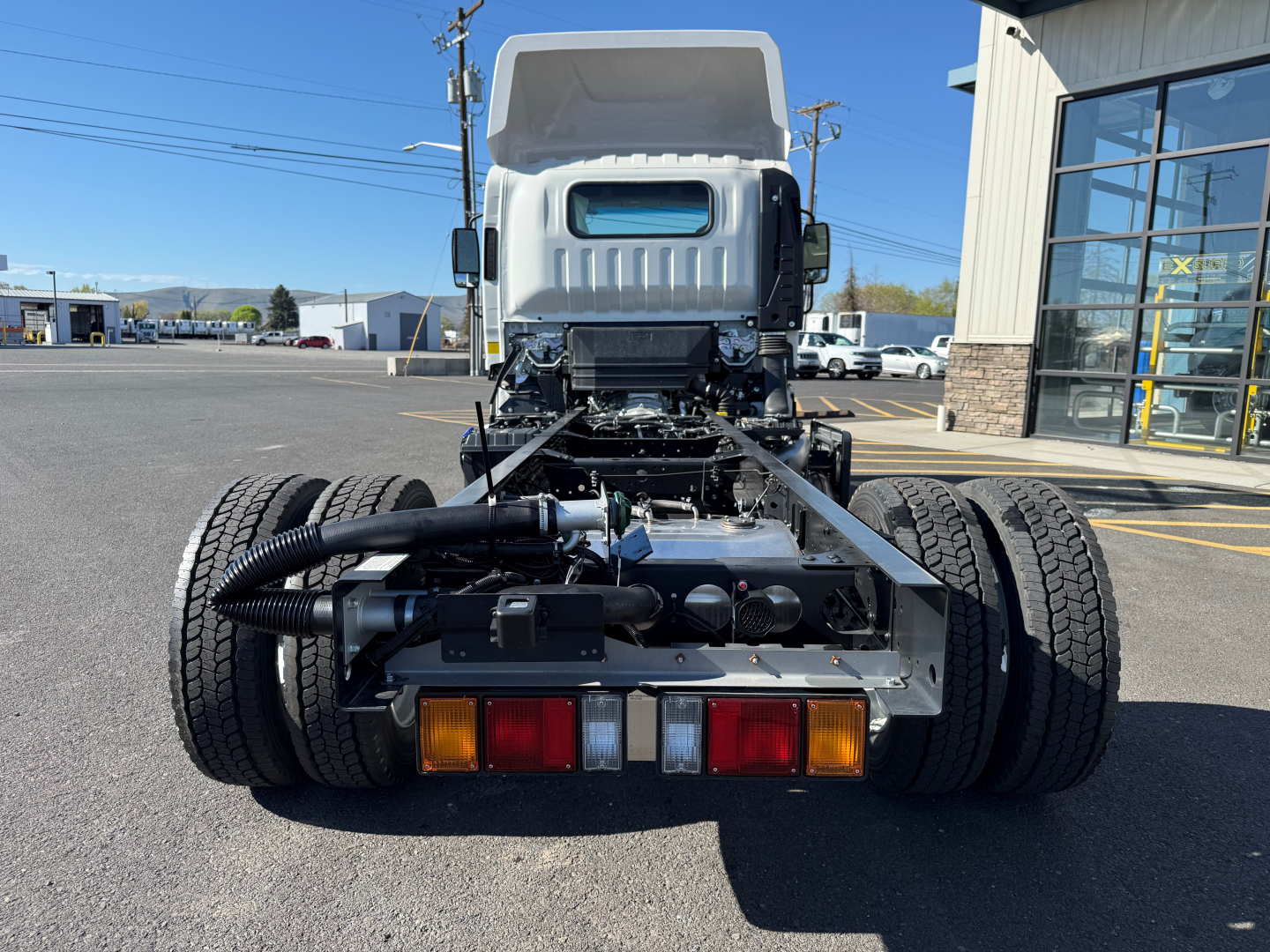 Isuzu NPRXD cab chassis rear view showing dual rear wheels, chassis frame, lights, and towing electrical connectors.
