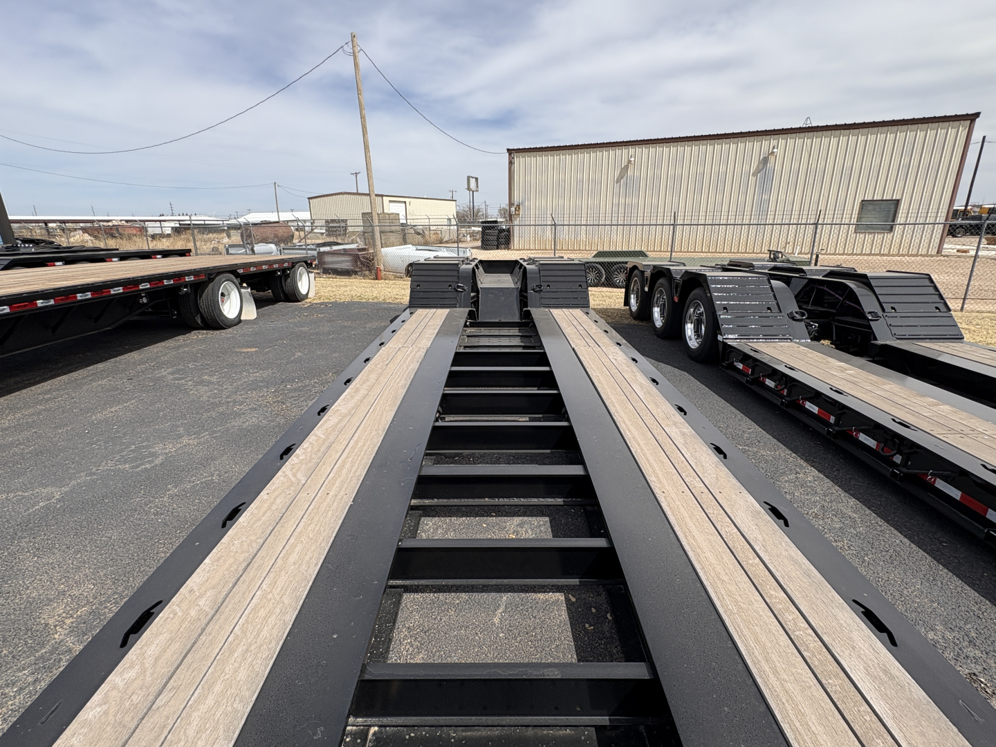 Load King trailer deck showing long lowboy frame with black uprights and light-colored wood deck sections, 9' 18" configuration, industrial yard.