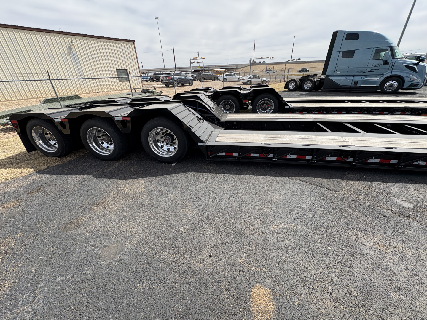 Load King lowboy trailer with triple-axle group showing aluminum deck and wheel hubs; 9' x 18' configuration, welded frame, loading ramps folded along deck.