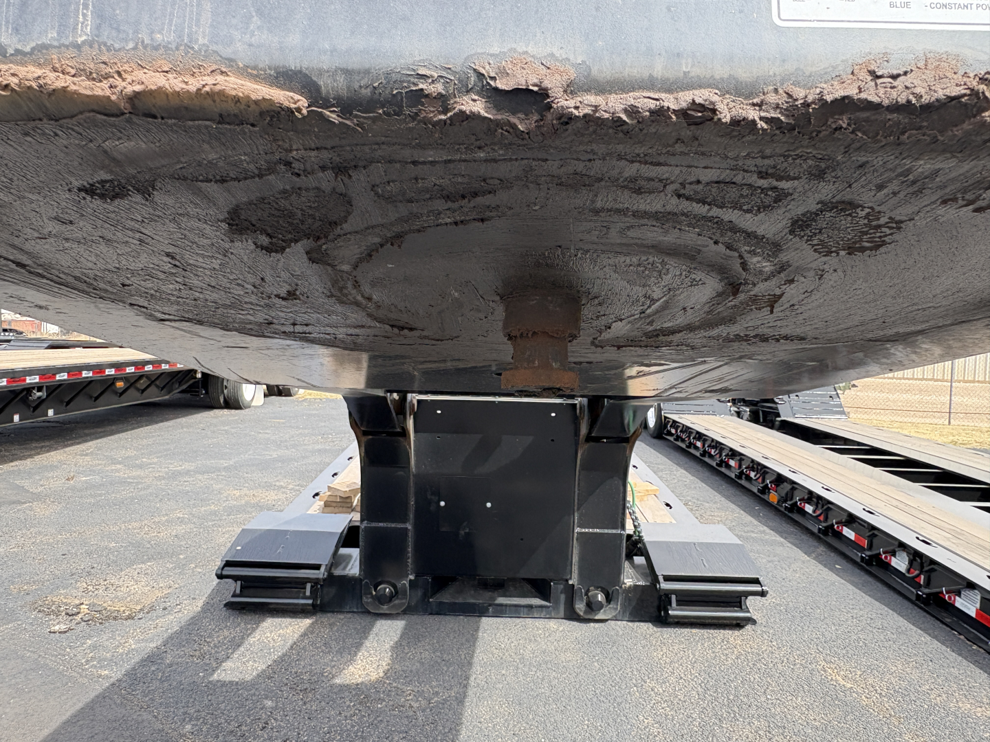Lowboy trailer undercarriage with steel support and mounting plates; underside detail of trailer frame and kingpin area.