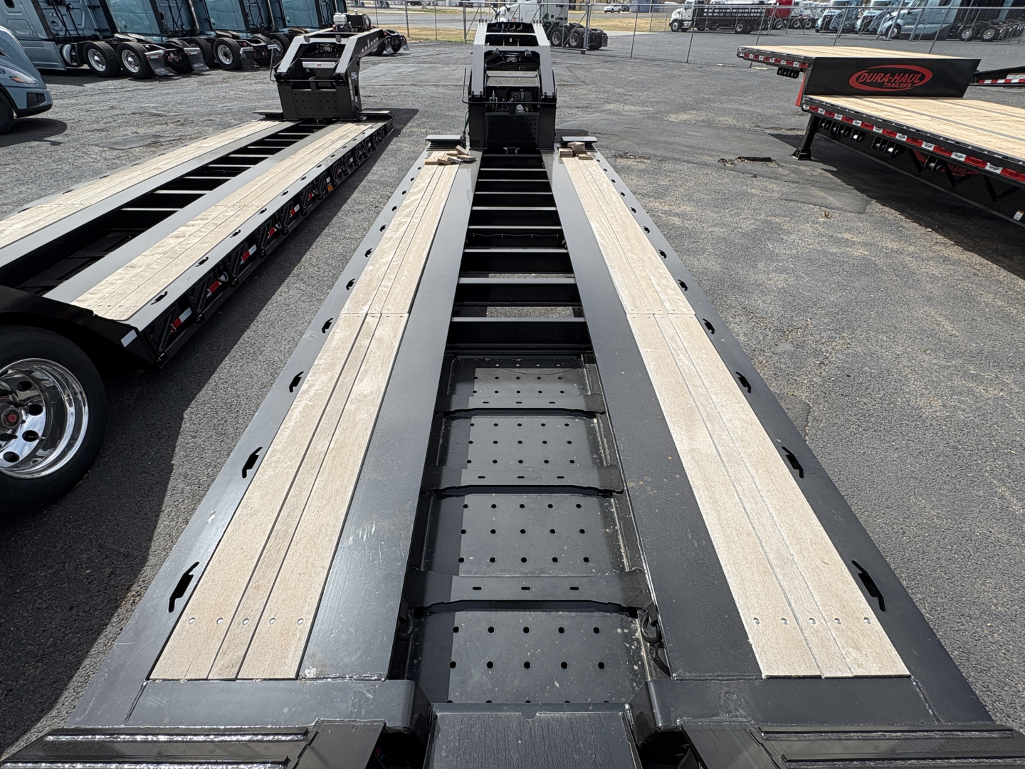 Load King lowboy trailer deck showing central spine with perforated stepping and side runway rails, long metal beams, wheel rests, and perforated tool access plates.