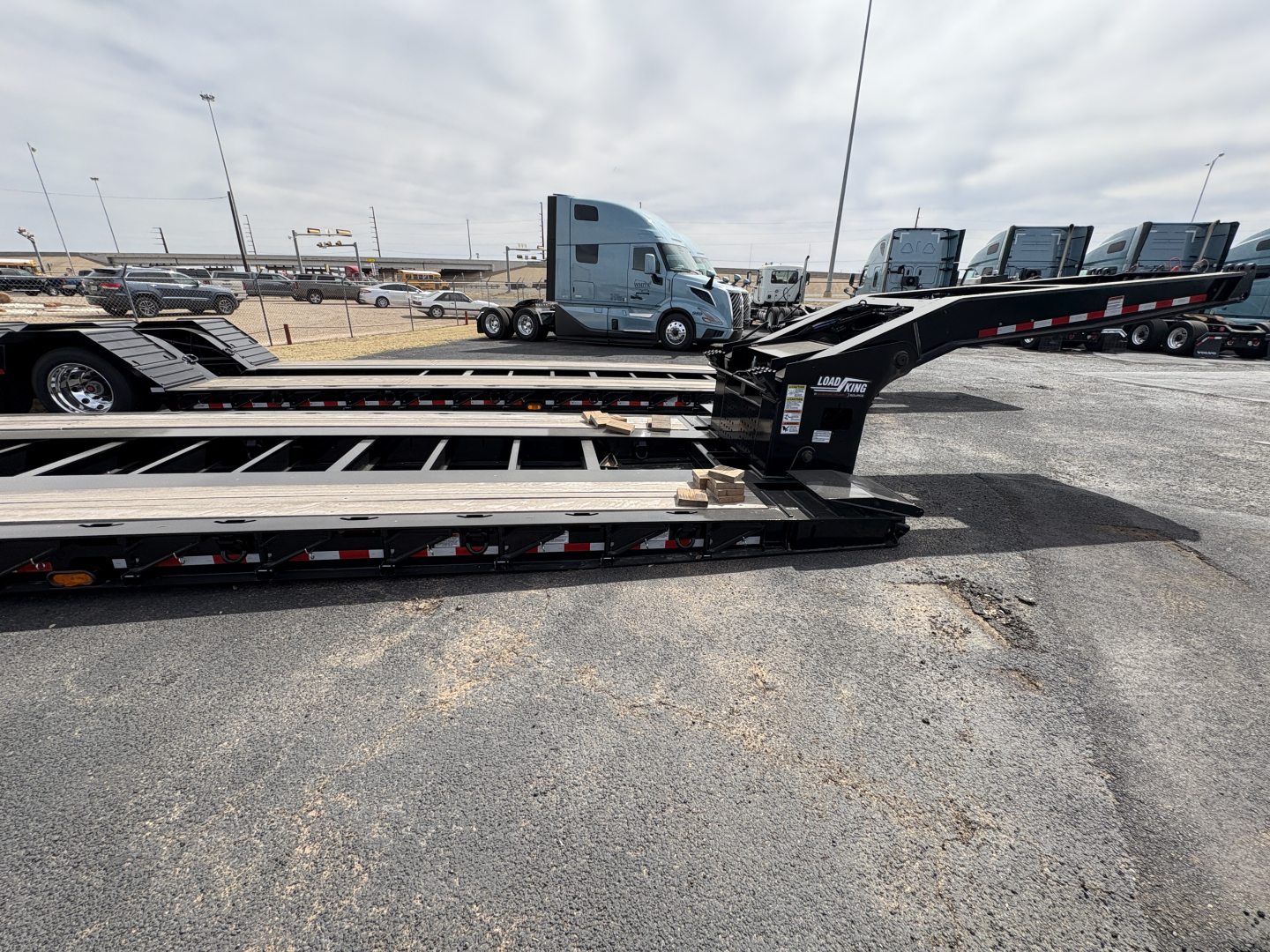 Load King trailer deck section with lowboy ramps and hitch, showing metal beams and warning decals.