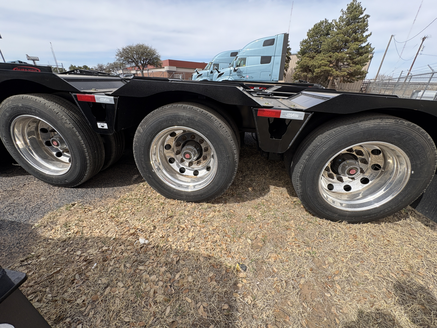 Load King trailer wheels and frame section showing triple axle with circular steel wheels and black structural beams.