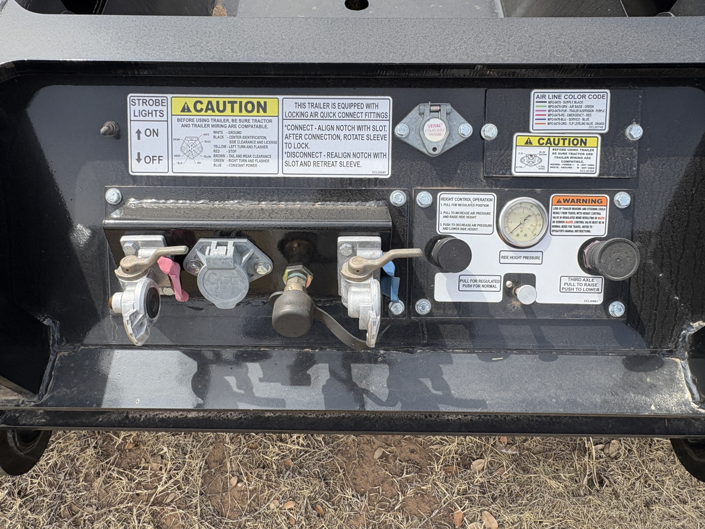 Trailer rear control panel showing strobe light switch, CAUTION labels, gauges, and valves on Load King lowboy trailer.