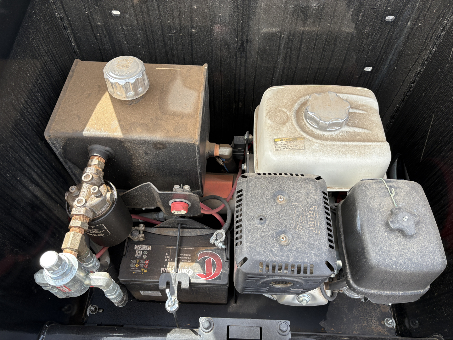 Trailer engine bay with two fuel tanks, a battery, and compact auxiliary components visible in a Load King trailer 9ft-18ft setup, showing fluid reservoirs and wiring