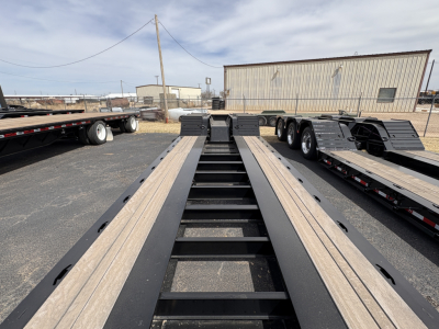 Load King trailer deck showing long lowboy frame with black uprights and light-colored wood deck sections, 9' 18" configuration, industrial yard.