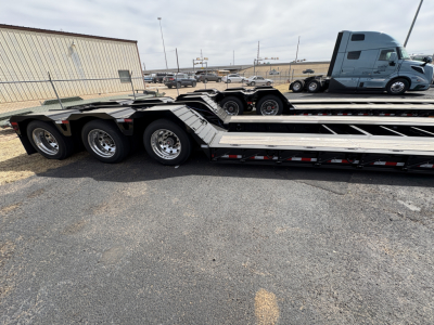 Load King lowboy trailer with triple-axle group showing aluminum deck and wheel hubs; 9' x 18' configuration, welded frame, loading ramps folded along deck.