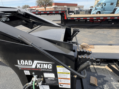 Load King trailer component showing decals and wiring with caution labels and a steel ramp; close view of the hitch area and deck frame.