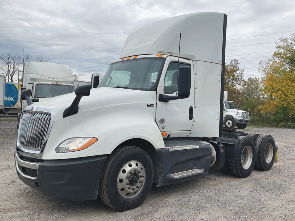 Truck in cab forward configuration showing International LT625 model with sleeper cab, side steps, dual rear axles, front grille, headlights, and white paint.