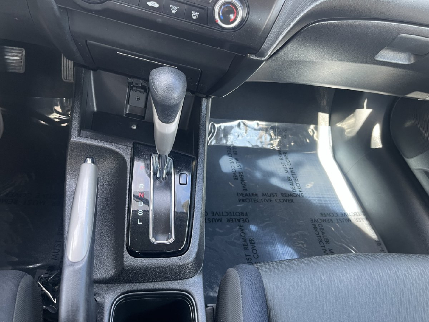 Interior view of a vehicle gear selector area showing automatic shifter with PRNDL indicators and surrounding console.