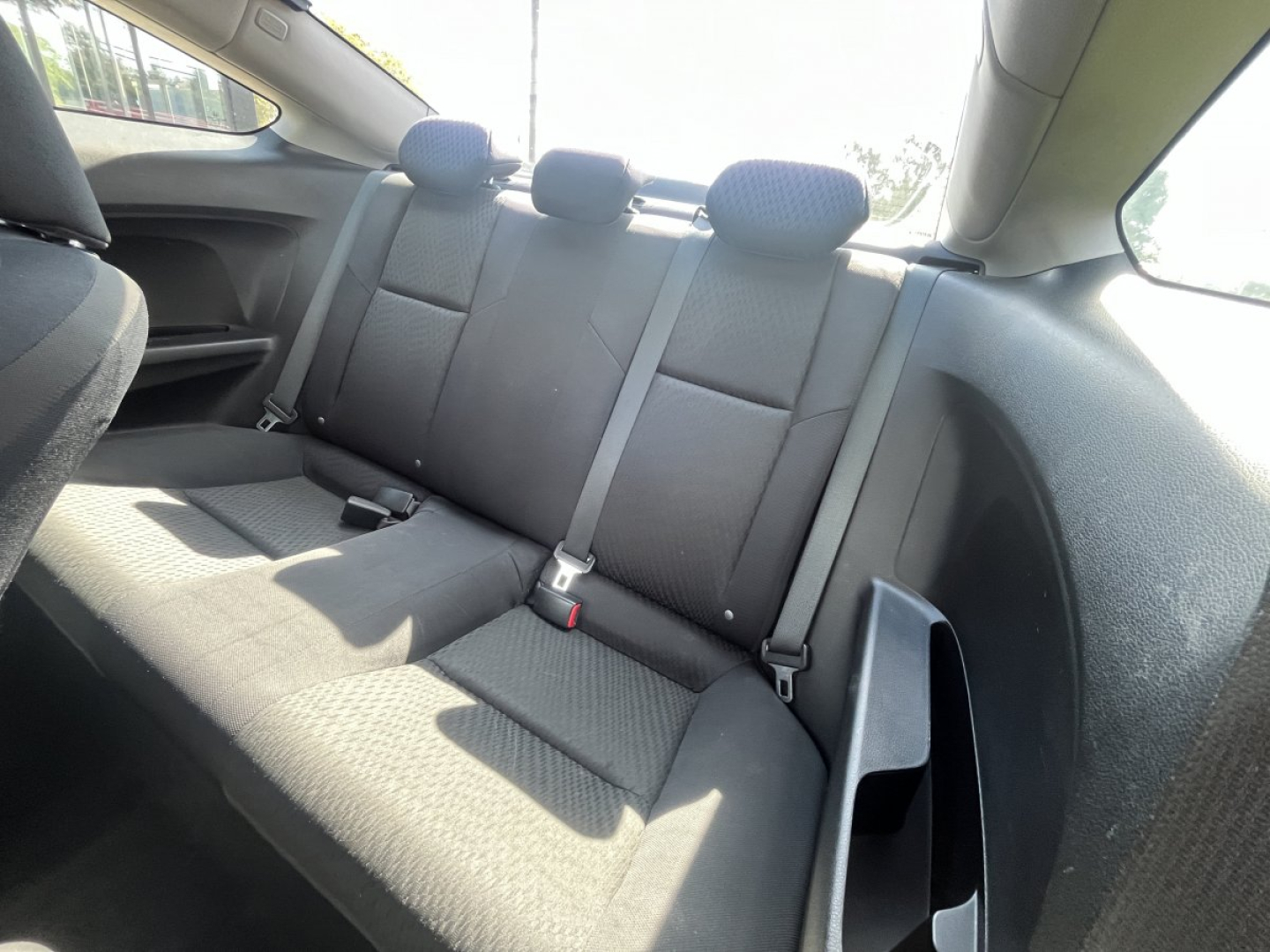 Trunk area of a 2015 Honda Civic Coupe showing rear seats with three headrests and seat belts in a compact car interior.