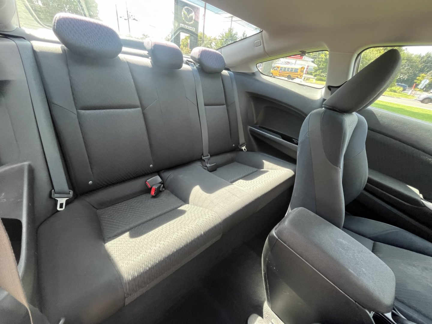 Car interior showing rear bench seats and front passenger seat in a 2015 Honda Civic Coupe; black fabric upholstery, three rear seat belts, headrests present.