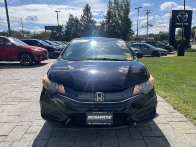 Front view of a 2015 Honda Civic Coupe in a dealership lot showing the front bumper, grille, headlights, and Honda emblem; windshield with sun glare and dealership license plate frame.
