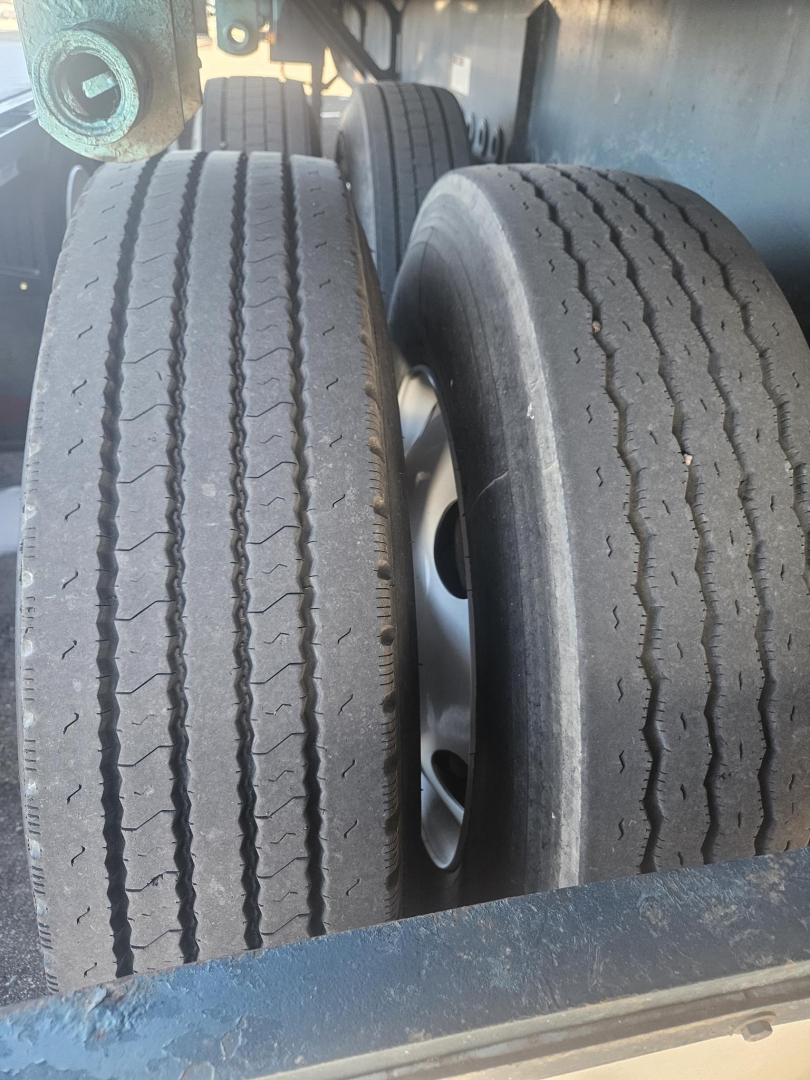 Two trailer tires on a flatbed trailer with visible tread patterns and rims; no legible branding or model text visible on tires from this angle.