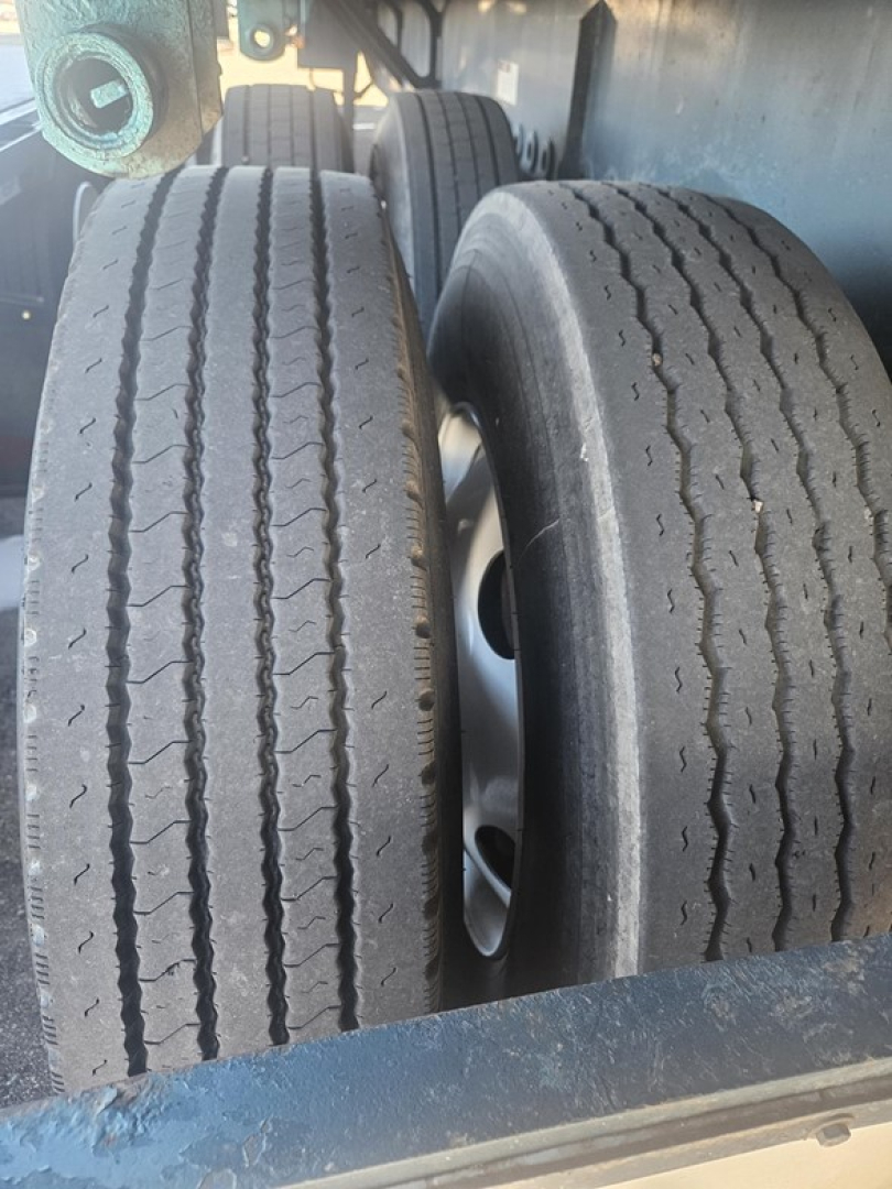 Flatbed trailer dual tires with tread visible, undercarriage and wheel wells; part of a Fruehauf steel flatbed trailer.