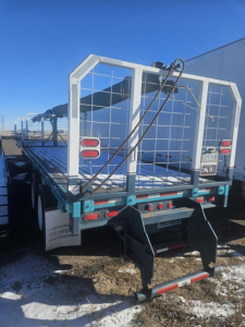 Flatbed trailer rear showing ramp and metal stake sides with safety chain and taillights; Fruehauf branding on fender and rear gate structure.