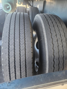 Flatbed trailer dual tires with tread visible, undercarriage and wheel wells; part of a Fruehauf steel flatbed trailer.