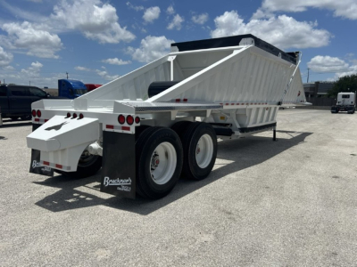 Dump trailer back view showing dual rear axles and raised dump bed with white and silver color and Beschner branding on mud flaps.