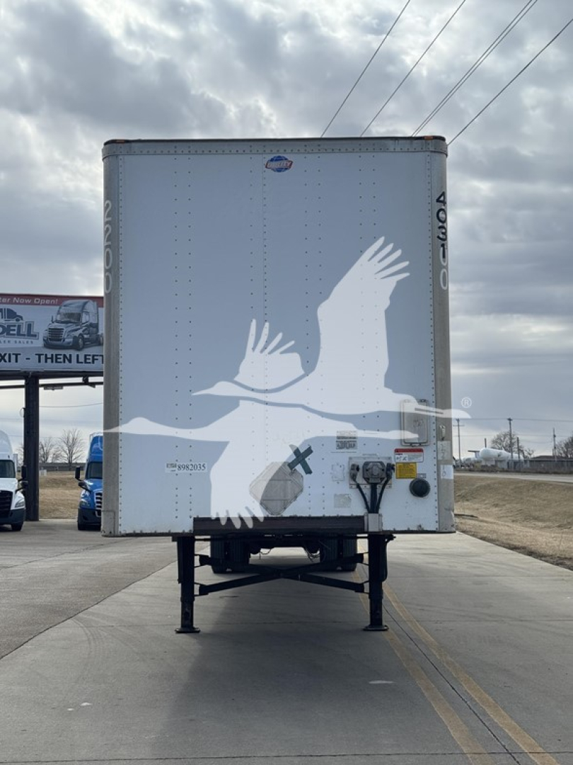 Rear view of a light-gray Utility 4000Dx trailer with a white bird graphic, supported by two stabilizing legs, parked on a road.