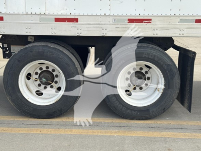 Two rear wheels of a trailer with dual-tire axle and white rims under a flatbed trailer.