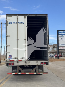 Utility trailer rear with open ramp doors, River Valley trailer logo on left door, white bird silhouette graphic on interior of trailer, taillights and bumper visible.