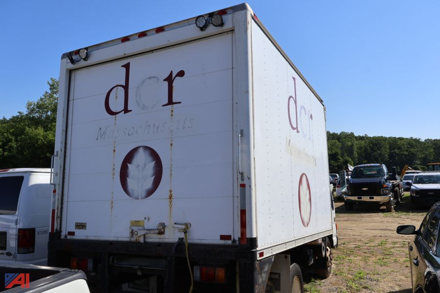 Box truck rear and side view showing cargo box with 'dr' logo and circular emblem, white exterior with side door, parked in a lot.