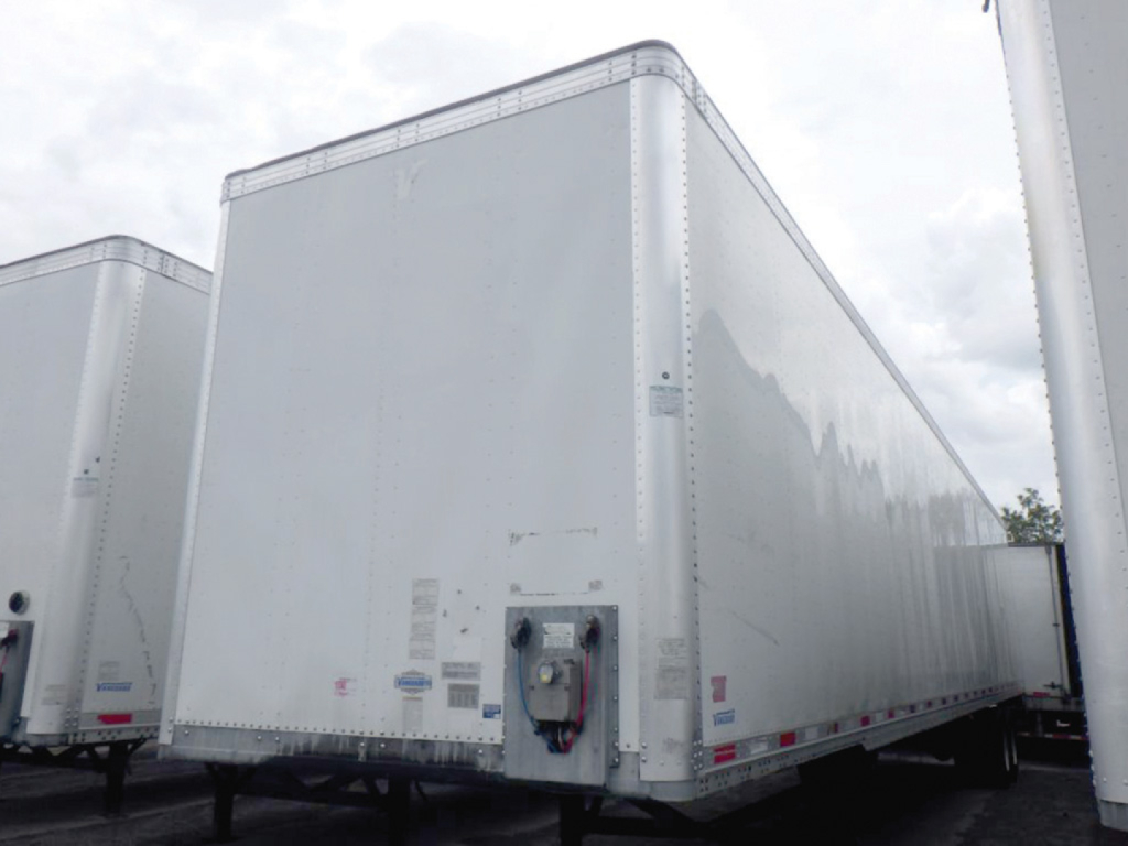 Trailer side showing rear door with hitch and labels on aluminum van trailer, white exterior, Vanguard van trailer in a yard.