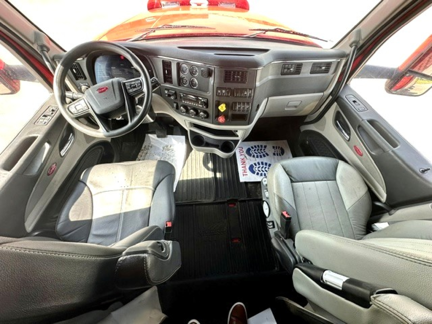 Interior view of a Peterbilt truck cockpit showing steering wheel, dashboard with gauges, center console, and driver/ passenger seats.
