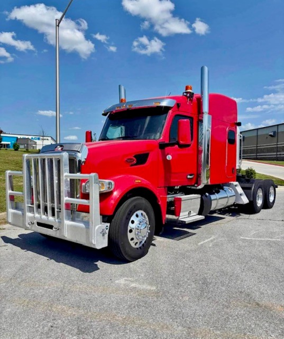 Peterbilt 567 conventional sleeper truck in red with front air dam and dual stacks, parked in a lot.