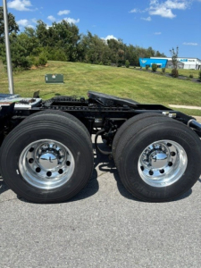 Peterbilt 567 chassis rear wheels and frame view showing chrome wheels and dual rear axles, in a parking lot.