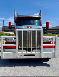 Peterbilt 567 conventional sleeper front view showing grille, bumper guard, headlights, and red mirrors.