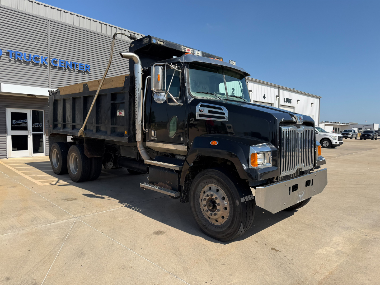 Dump truck with Western Star grille showing black cab and dump bed in a dealership lot. Visible text includes 'TRUCK CENTER' on building, and various stickers on the door area and cab window. Vehicle details on listing include VIN 5KKHAVDV3