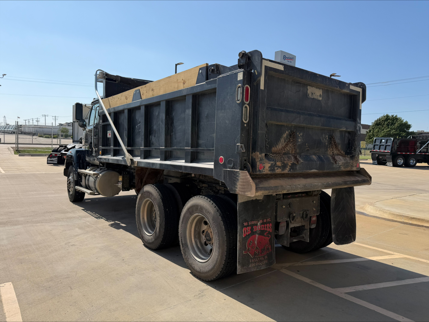Dump truck showing rear and side view with dirt-covered bed and taillights. Visible text includes 'DP' on mudflap and reflective markings; no other legible labels.