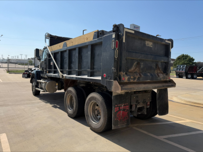 Dump truck showing rear and side view with dirt-covered bed and taillights. Visible text includes 'DP' on mudflap and reflective markings; no other legible labels.