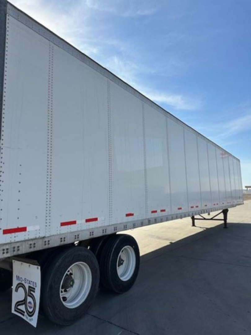 Trailer side view showing a white Wabash van trailer with dual rear wheels and red reflective tape.