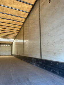 Trailer interior showing empty cargo area with wooden ceiling slats and aluminum side walls; long length perspective.