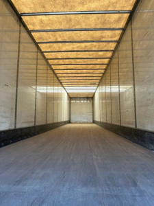 Trailer interior showing long empty cargo area with wooden roof beams, side walls, and dark floor in a Wabash van trailer.