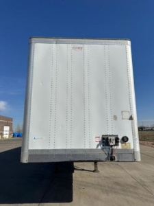 Rear view of a white box trailer with a fiberglass front and lower steel rail. Rear doors closed; trailer hitch and electrical connections visible at bottom center.
