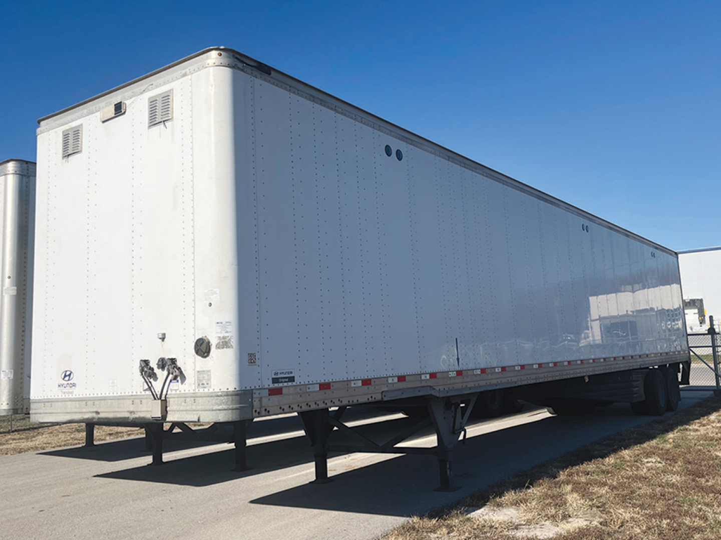 Long white trailer showing side view with dual axles and landing gear.
